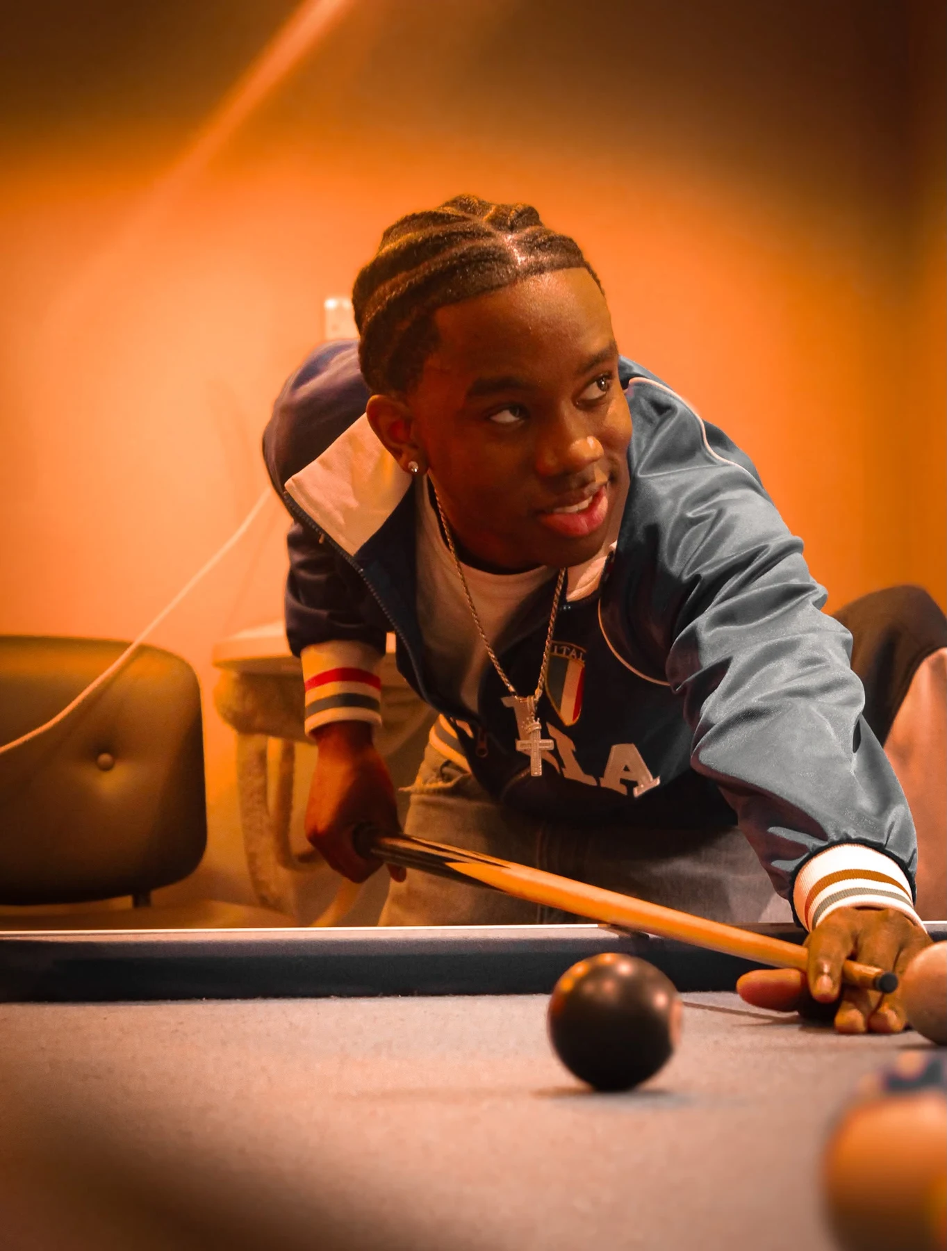 Ladi leaning across a pool table under warm orange light